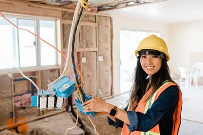 Électricienne casquée intervenant sur un tableau en chantier